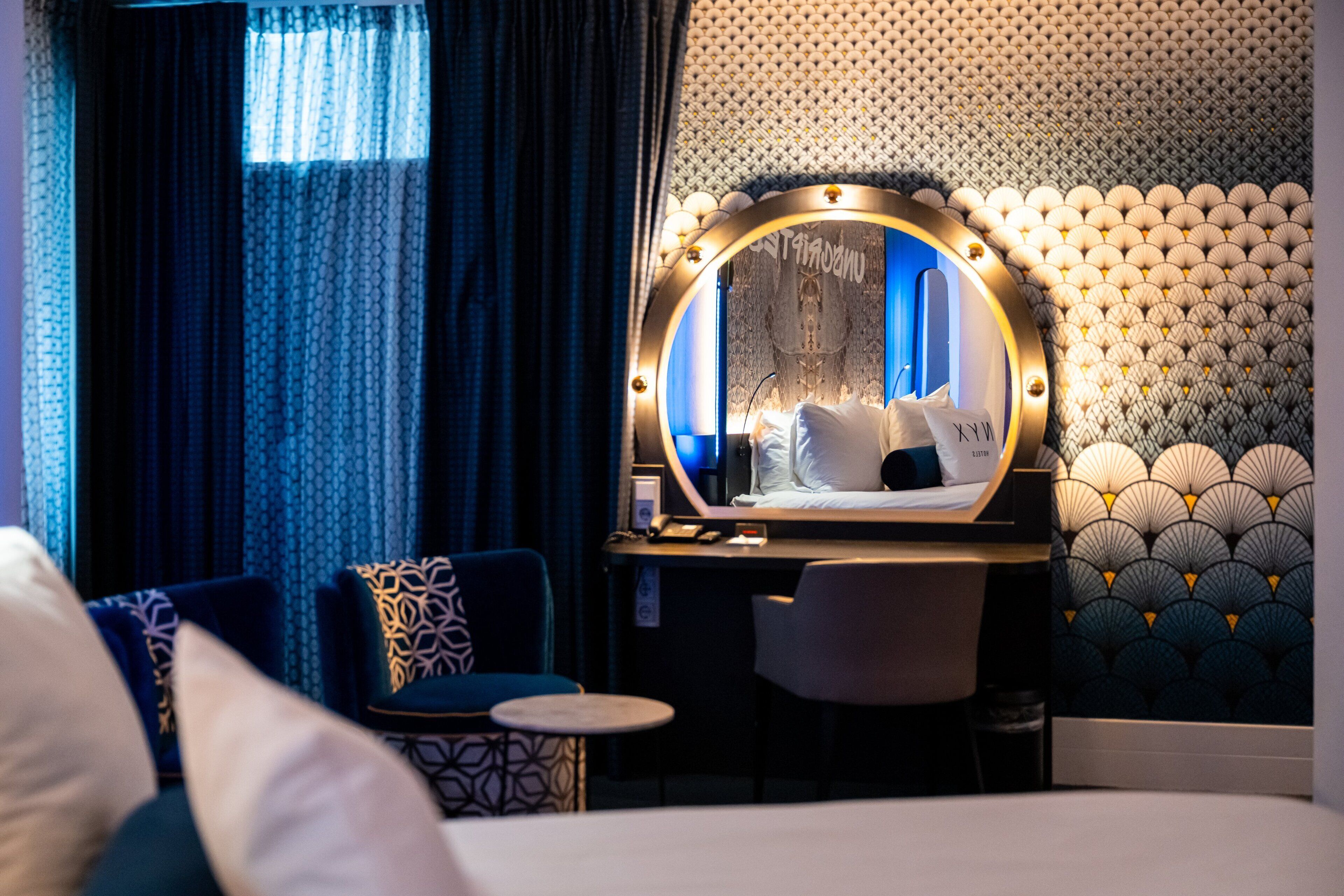 A hotel room with a bed, a desk with a mirror, a chair, and a round table.