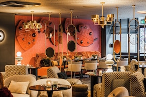 A modern interior with patterned furniture, a large leaf mural, and multiple hanging light fixtures. - NYX Hotel Amsterdam Rembrandt Square (Amsterdam)