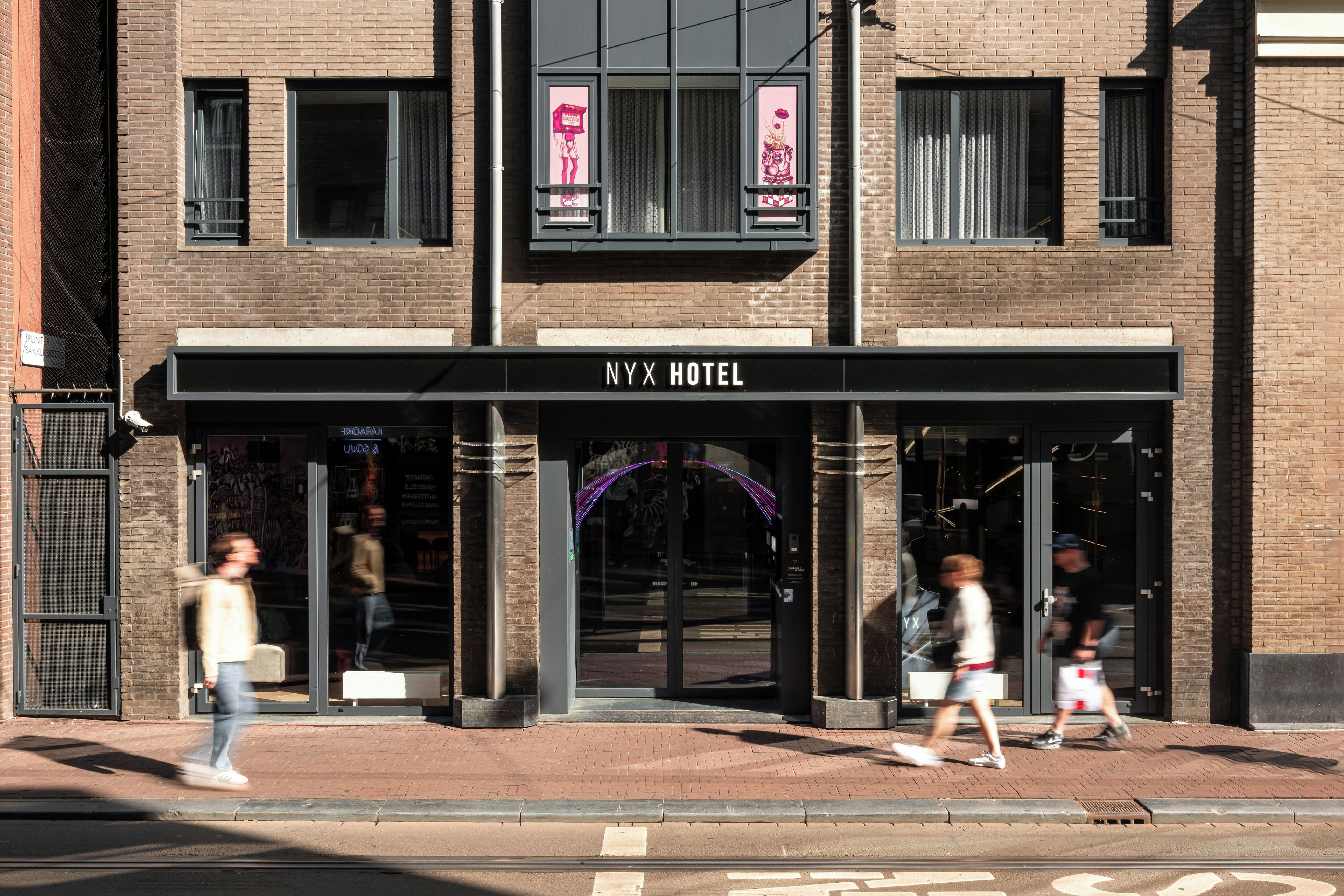 The NYX HOTEL entrance with a clear sign, a glass door, and a pedestrian crossing the street.