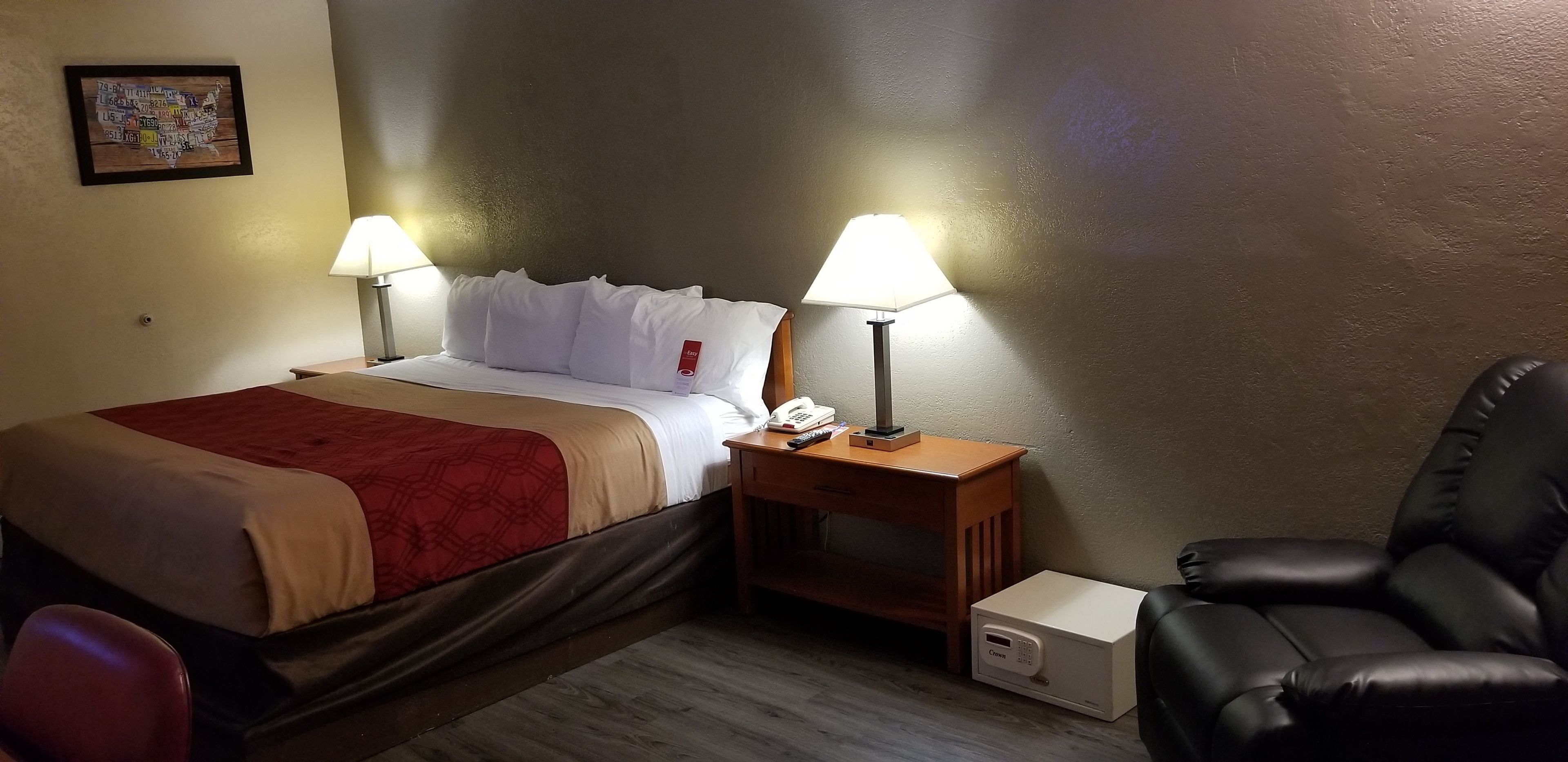 A hotel room with a bed, two bedside lamps, a desk with a telephone, a black leather chair, and a small white box.