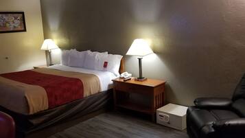 Une chambre d’hôtel avec un lit, deux lampes de chevet, un bureau avec un téléphone, un fauteuil en cuir noir et une petite boîte blanche.