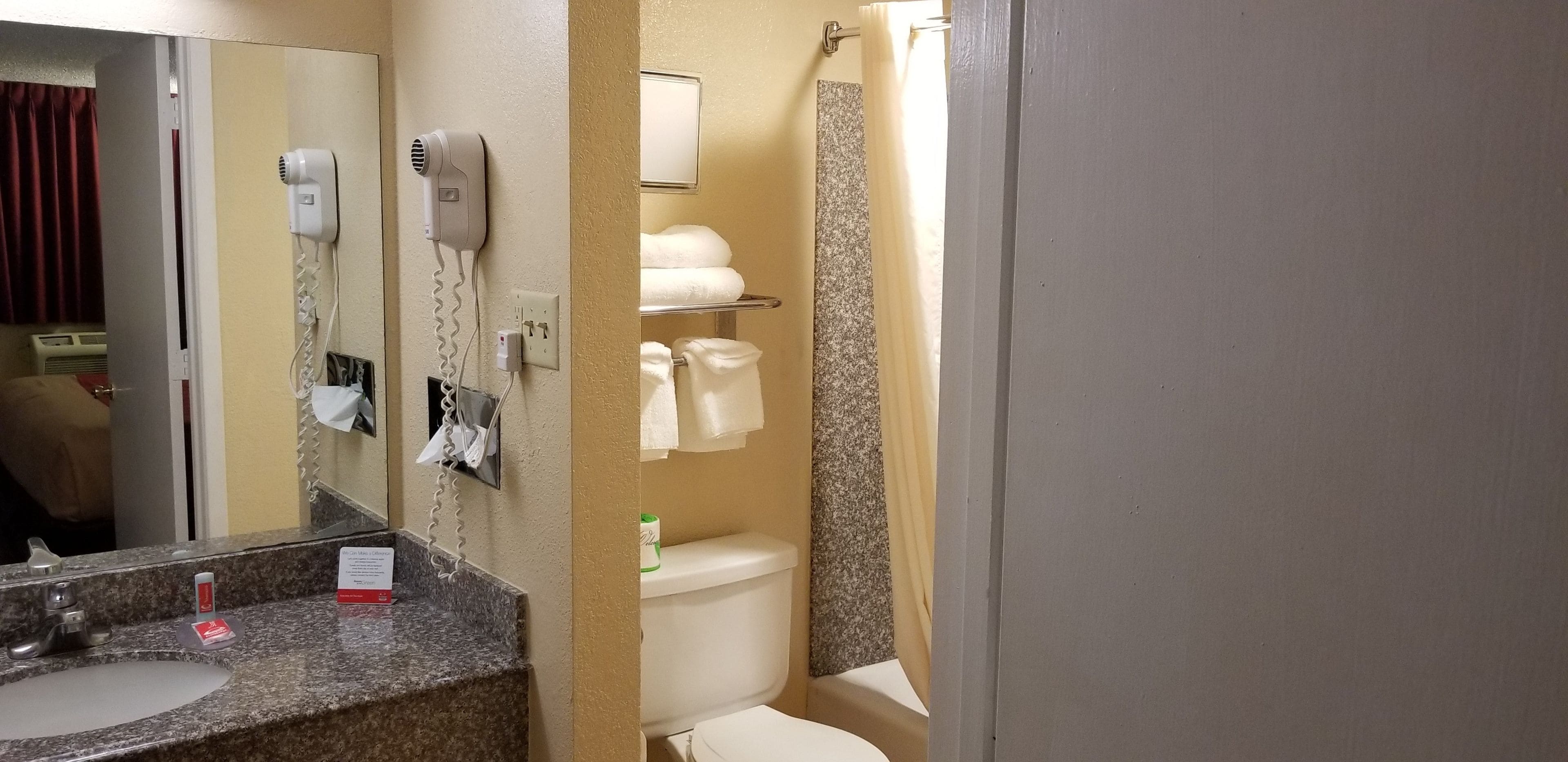 Une salle de bain dotée d’un comptoir en granit, d’un lavabo, d’un sèche-cheveux, d’un miroir, de toilettes et d’un rideau de douche.