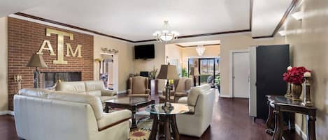 A spacious living room with a fireplace, leather sofas, a glass coffee table, and a chandelier.