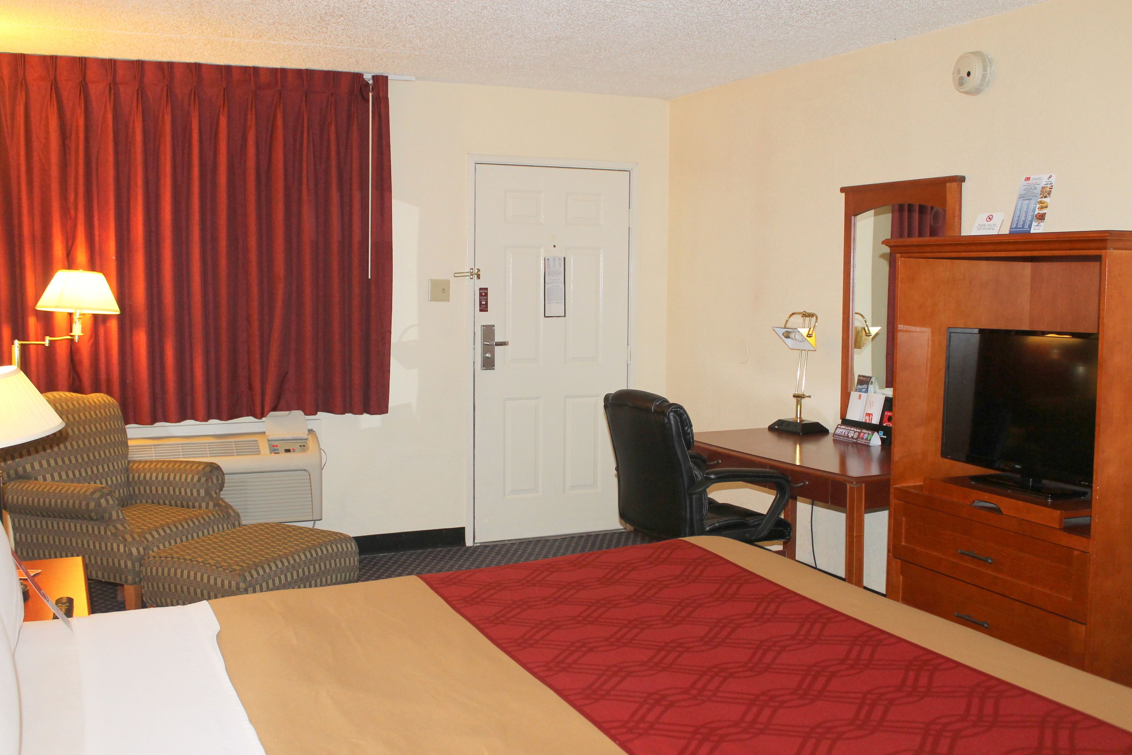 Ein Hotelzimmer mit Bett, Schreibtisch, Fernseher, Stuhl und einem roten Vorhang.
