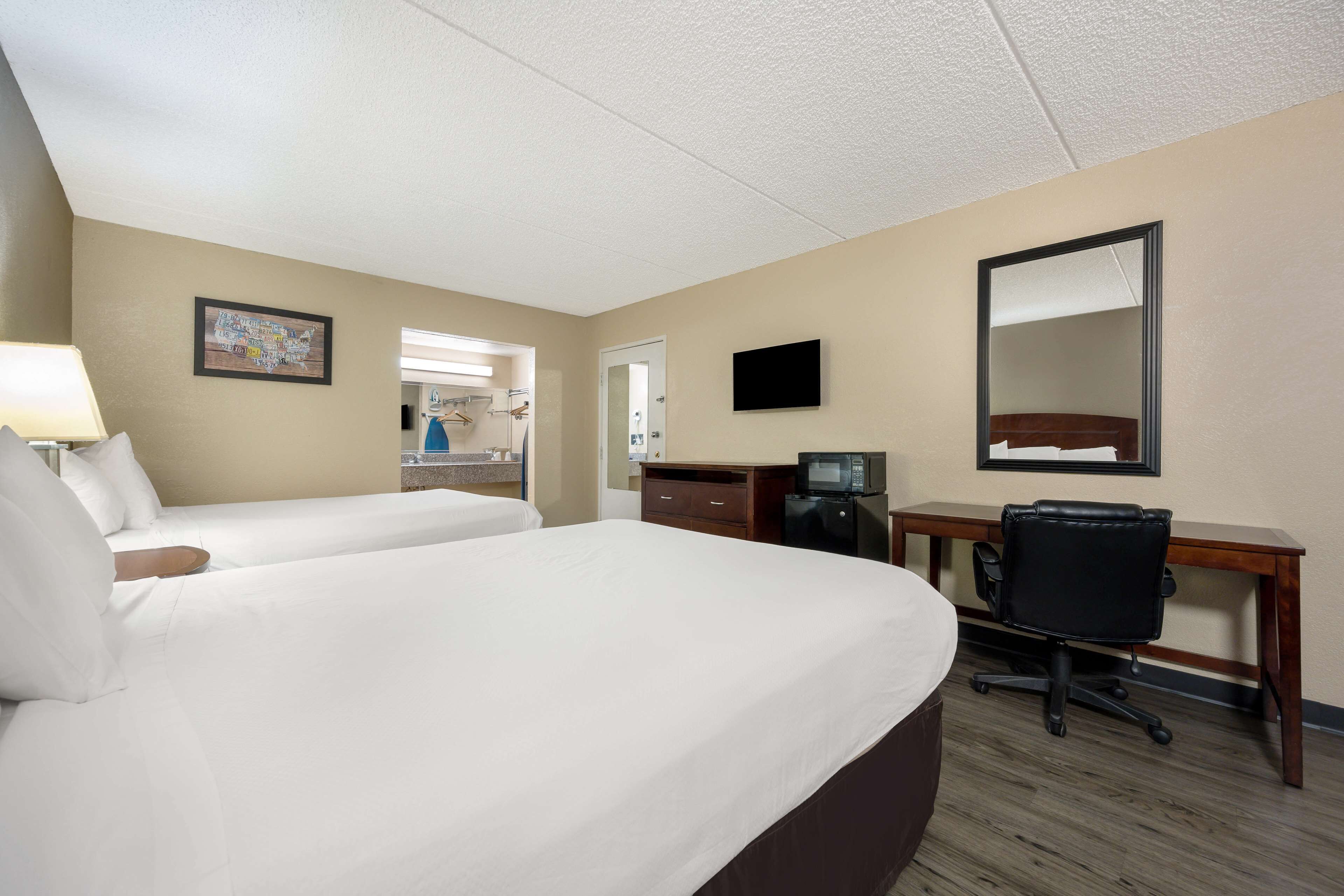 A hotel room with two single beds, a desk with a chair, a television, a coffee maker, and a mirror.