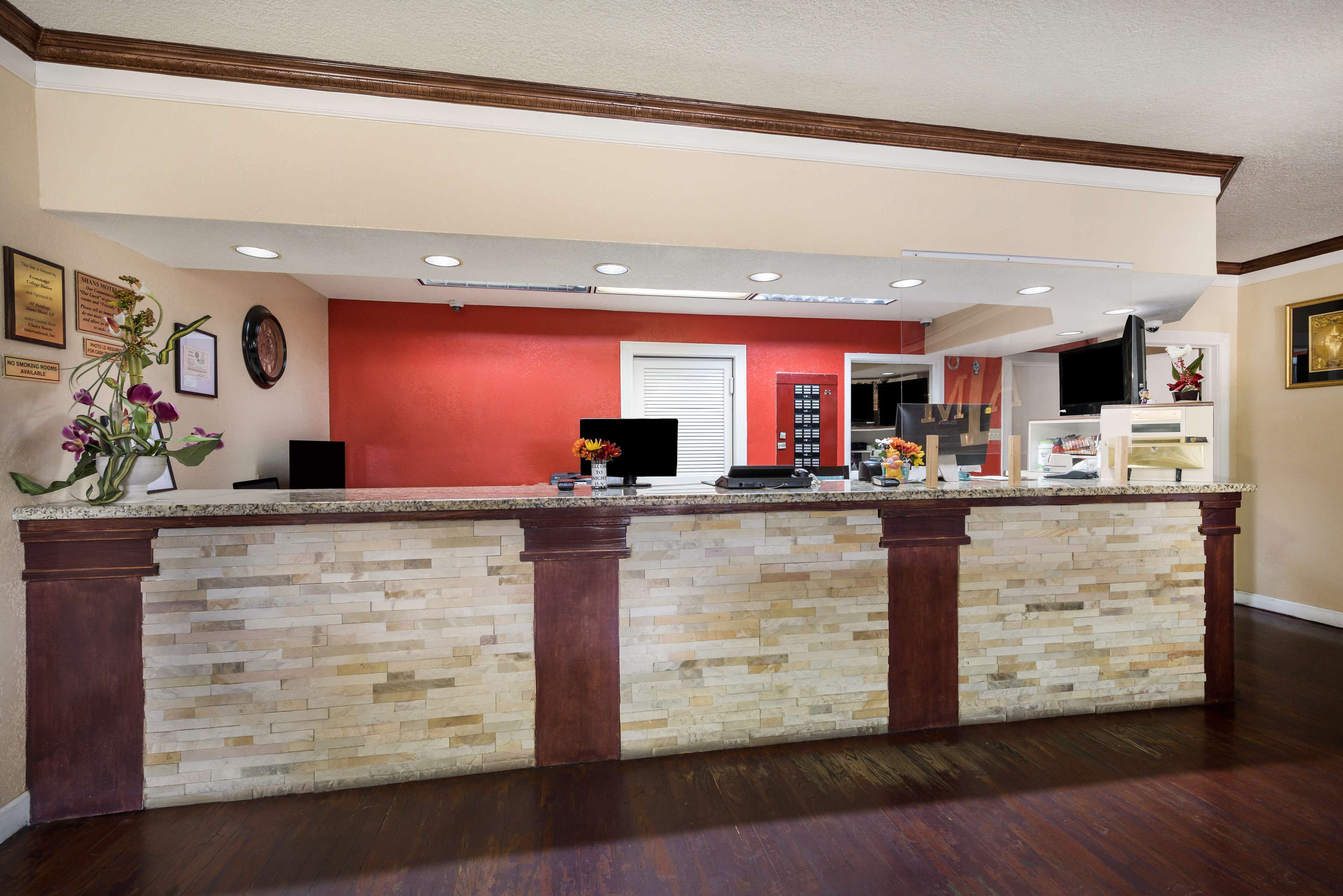 A reception area with a stone counter, wooden columns, a red accent wall, and a flat-screen TV.