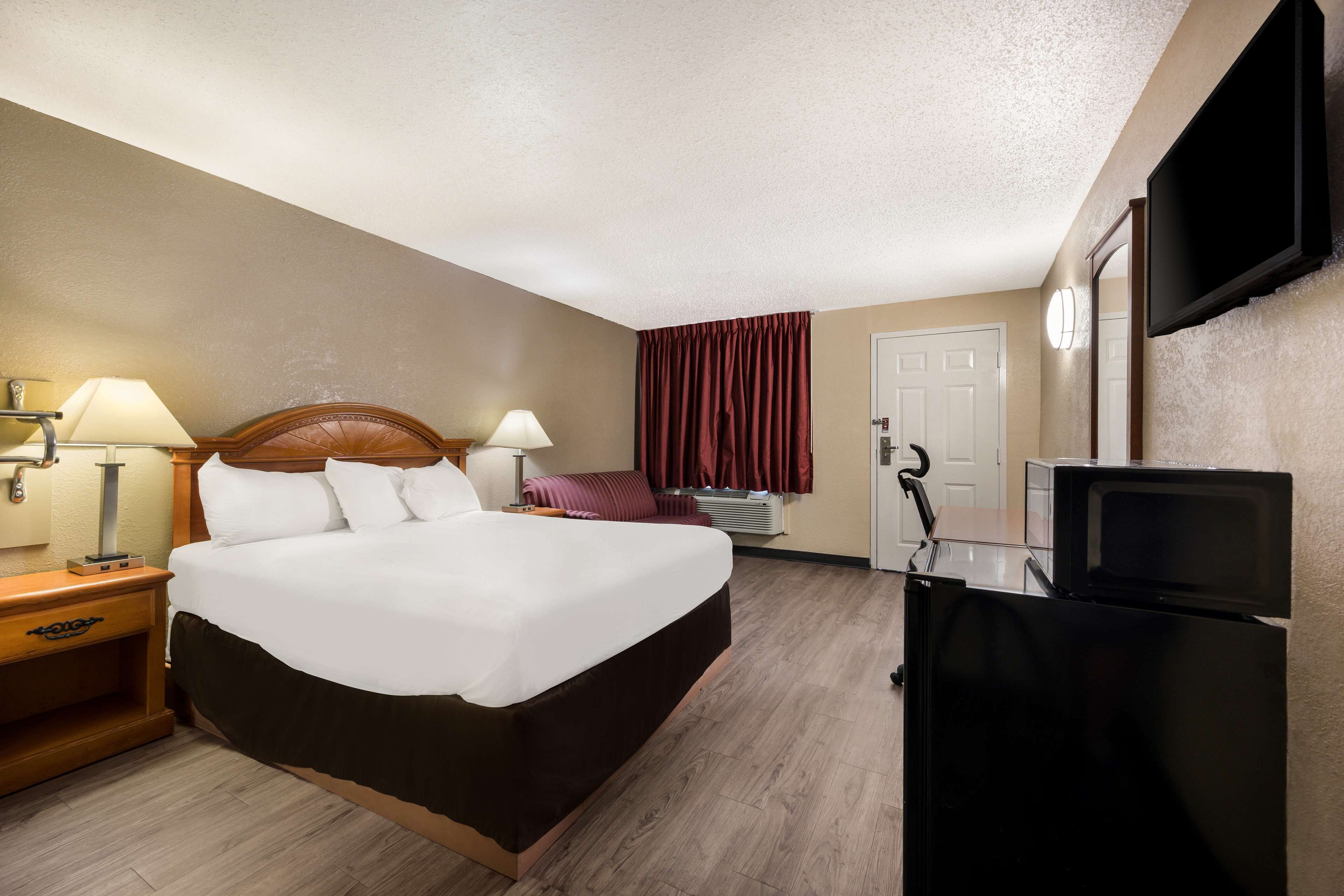 A hotel room with a large bed, two bedside lamps, a flat-screen TV, a microwave, and a door with a curtain.