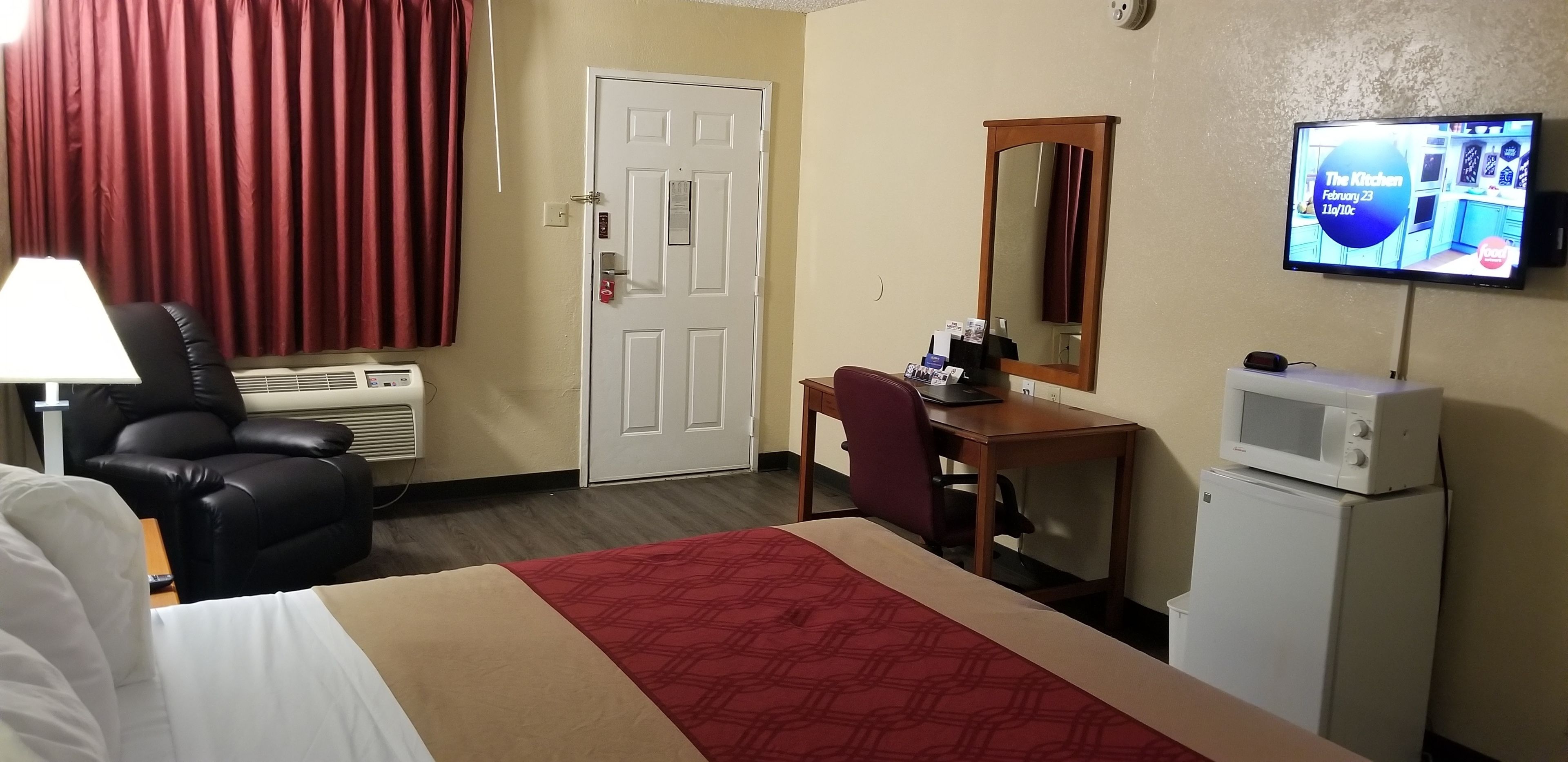 A hotel room with a bed, a desk, a chair, a television, a microwave, and a door.