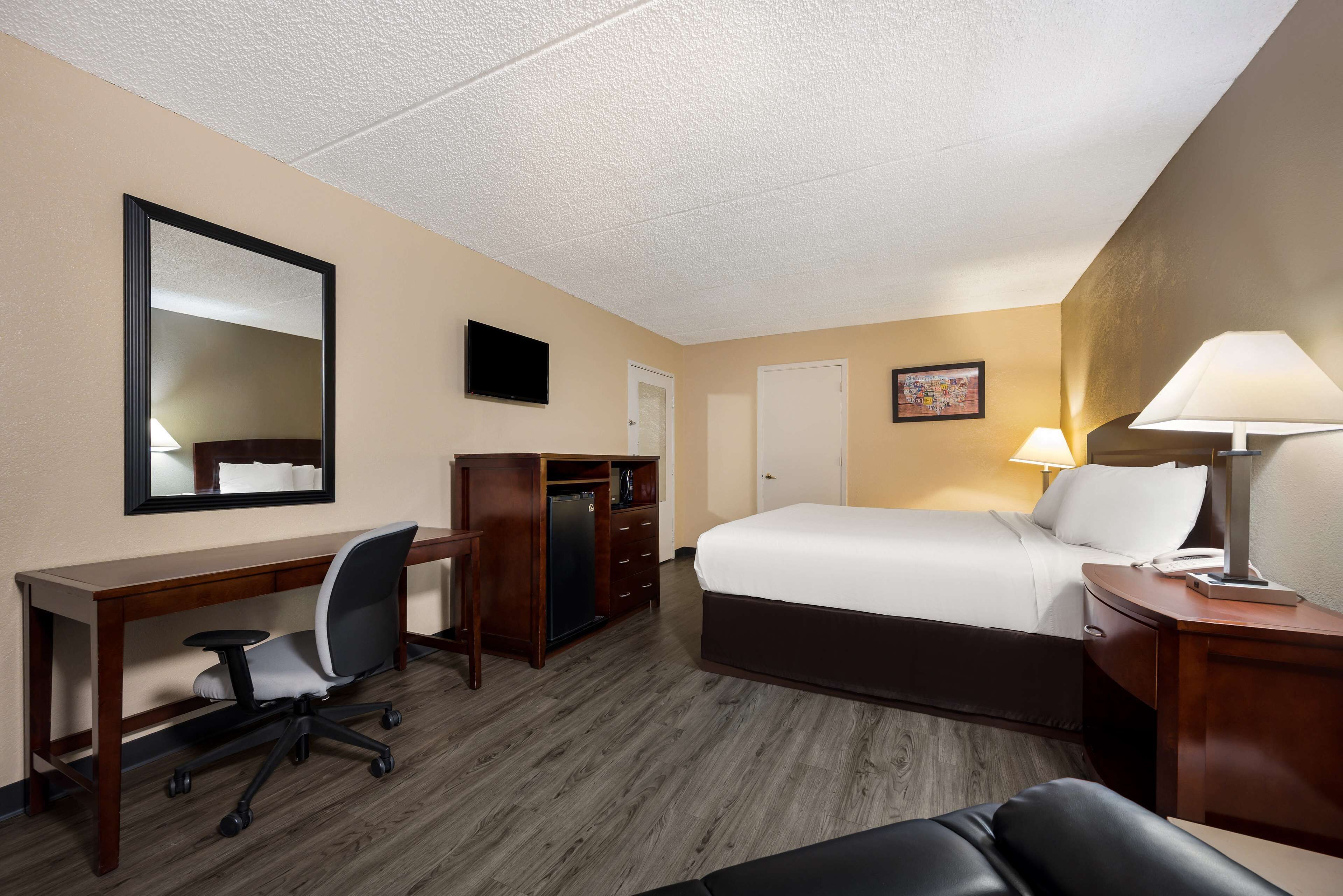 A hotel room with a bed, desk, chair, dresser, and a television on the wall.