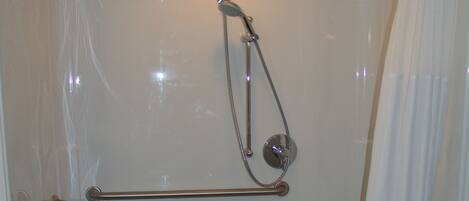 A walk-in shower with a grab bar, a showerhead, and a curtain.