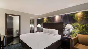 Habitación de hotel con una cama grande, dos mesitas de noche con lámparas, una silla y un mural en la pared que representa un paisaje forestal.