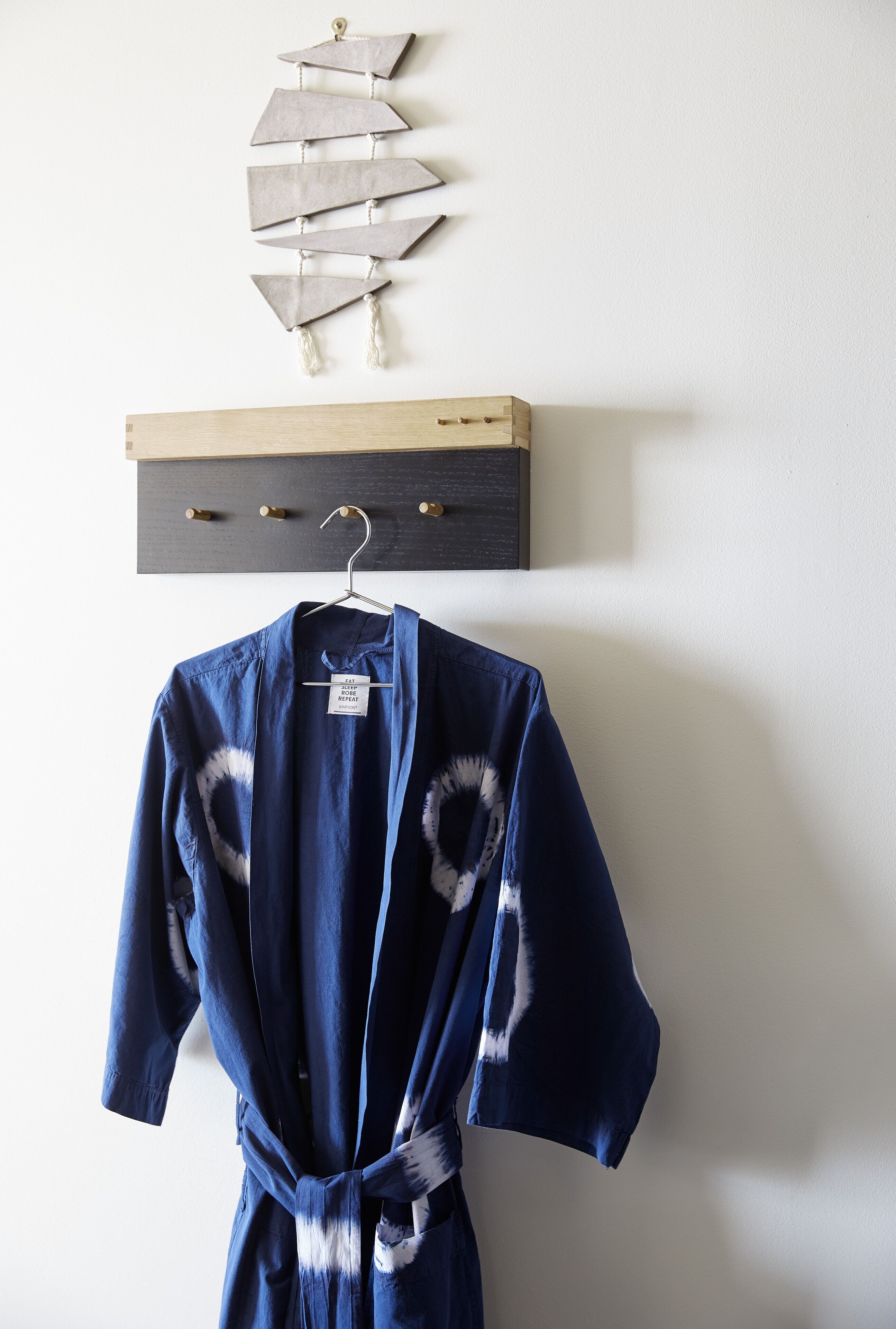 A blue robe hanging on a wooden rack against a white wall, with a decorative wall hanging above it.