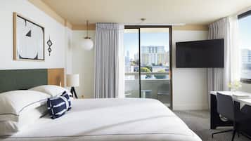 Une chambre d’hôtel avec un lit, un bureau, une télévision et un balcon donnant sur la ville.