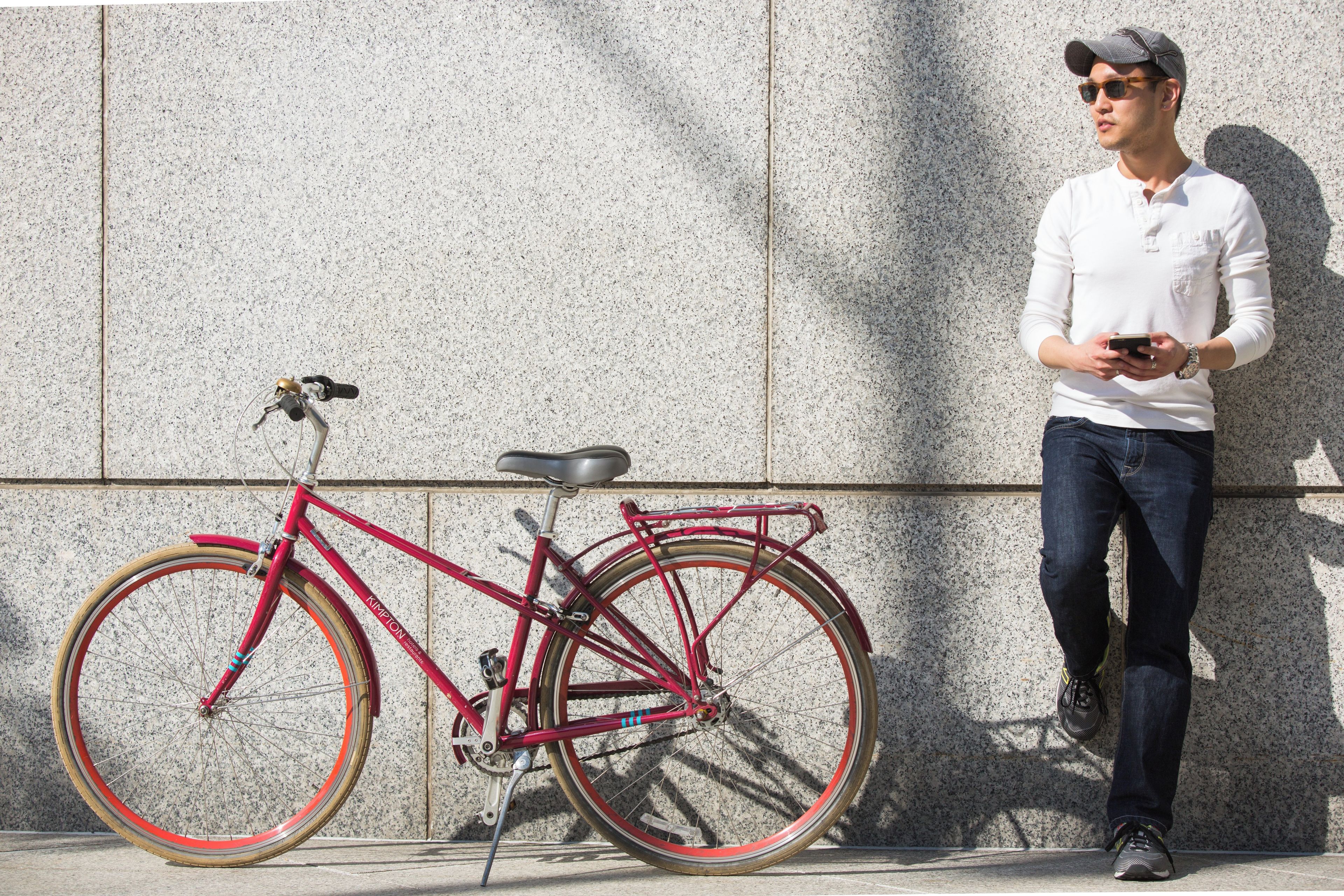 A person standing next to a red bicycle with a chain and gears, leaning against a textured wall.