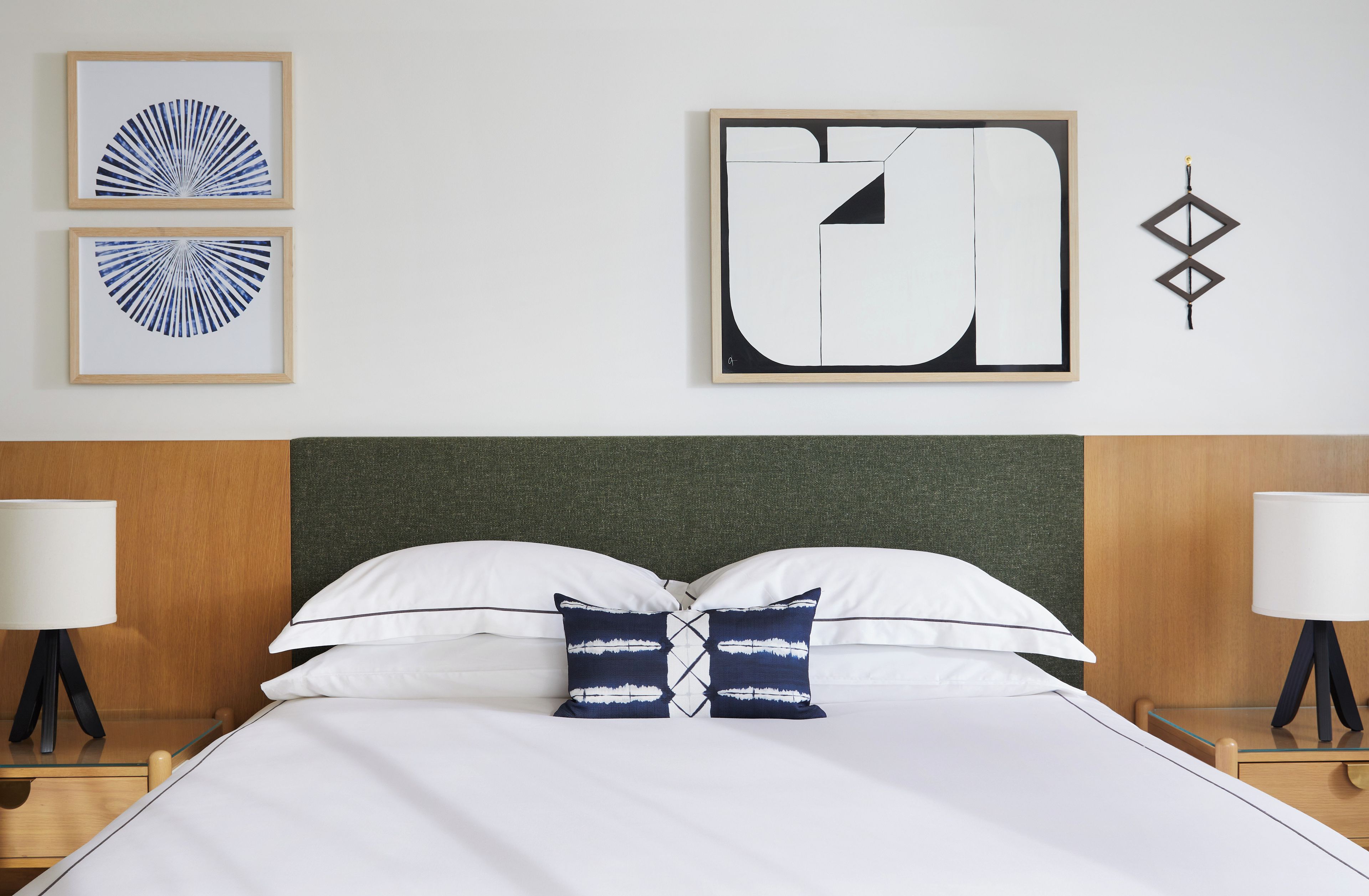Une chambre d’hôtel comprenant un lit, deux tables de chevet, une petite table, une lampe fixée au mur et deux œuvres d’art encadrées.