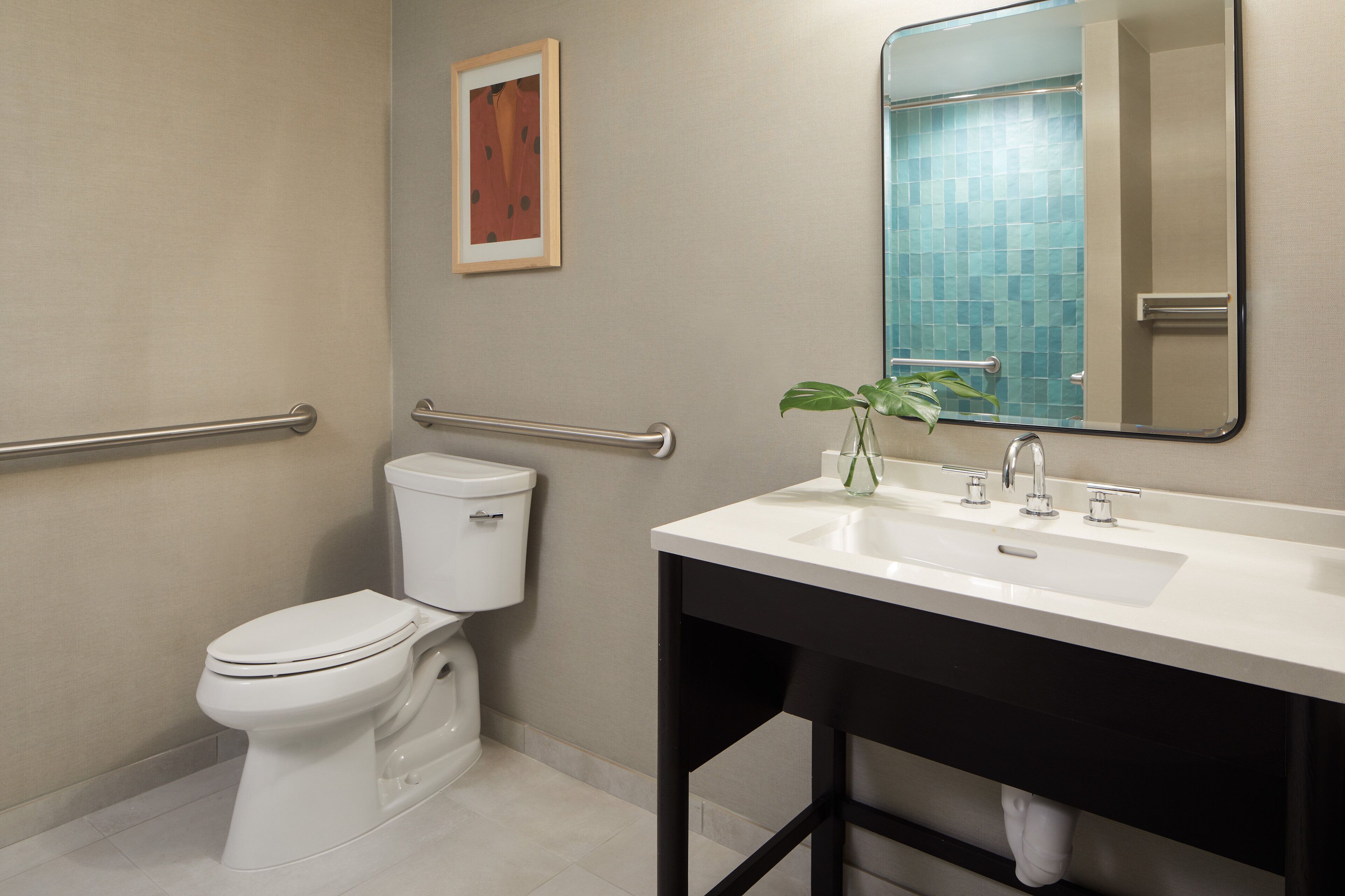 A modern bathroom with a toilet, a sink, a mirror, and a handrail.