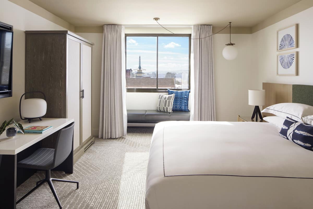 A hotel room with a large bed, a desk with a chair, a TV, and a window with curtains.