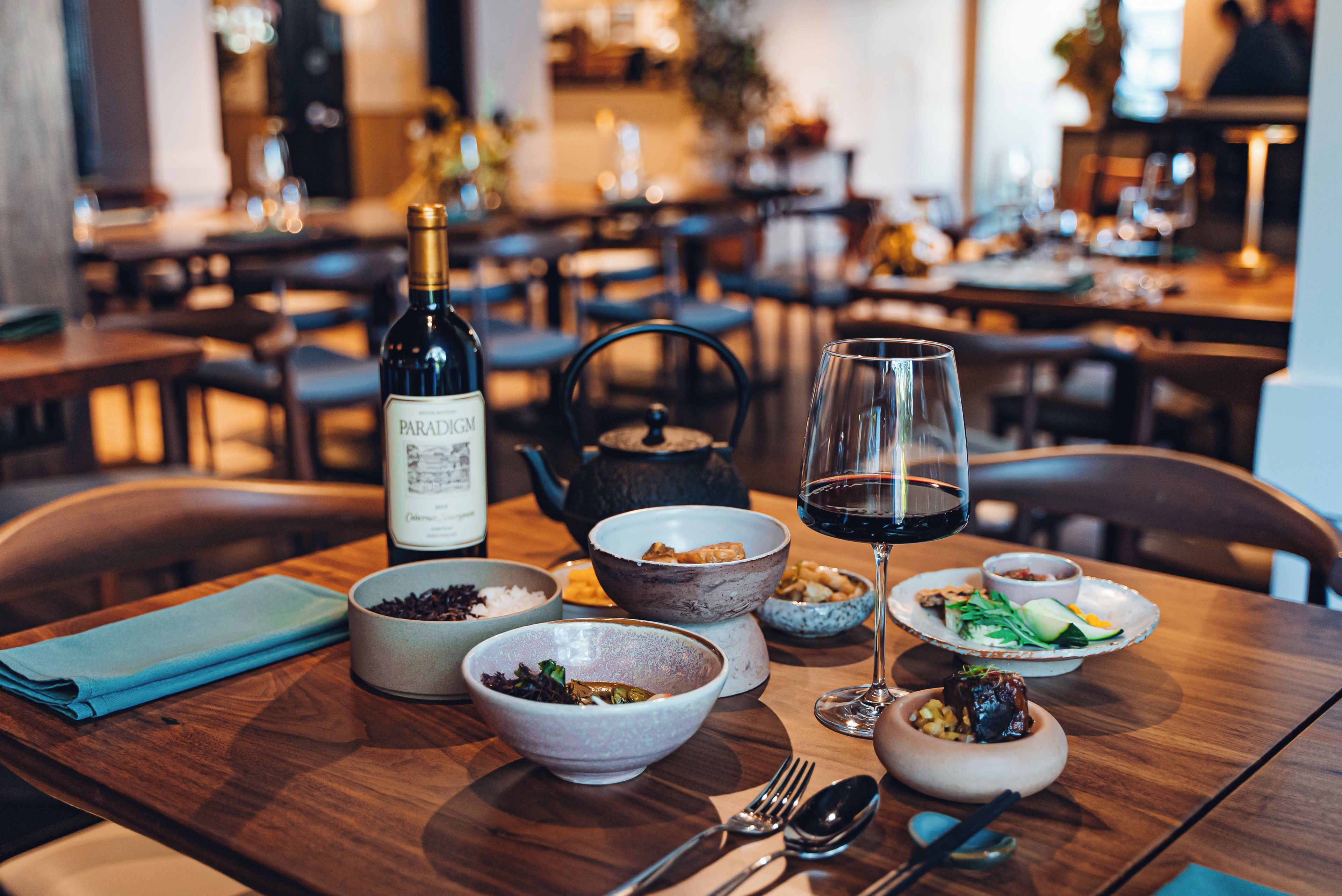Une table à manger dressée avec différents plats, une bouteille de vin et un verre de vin rouge.