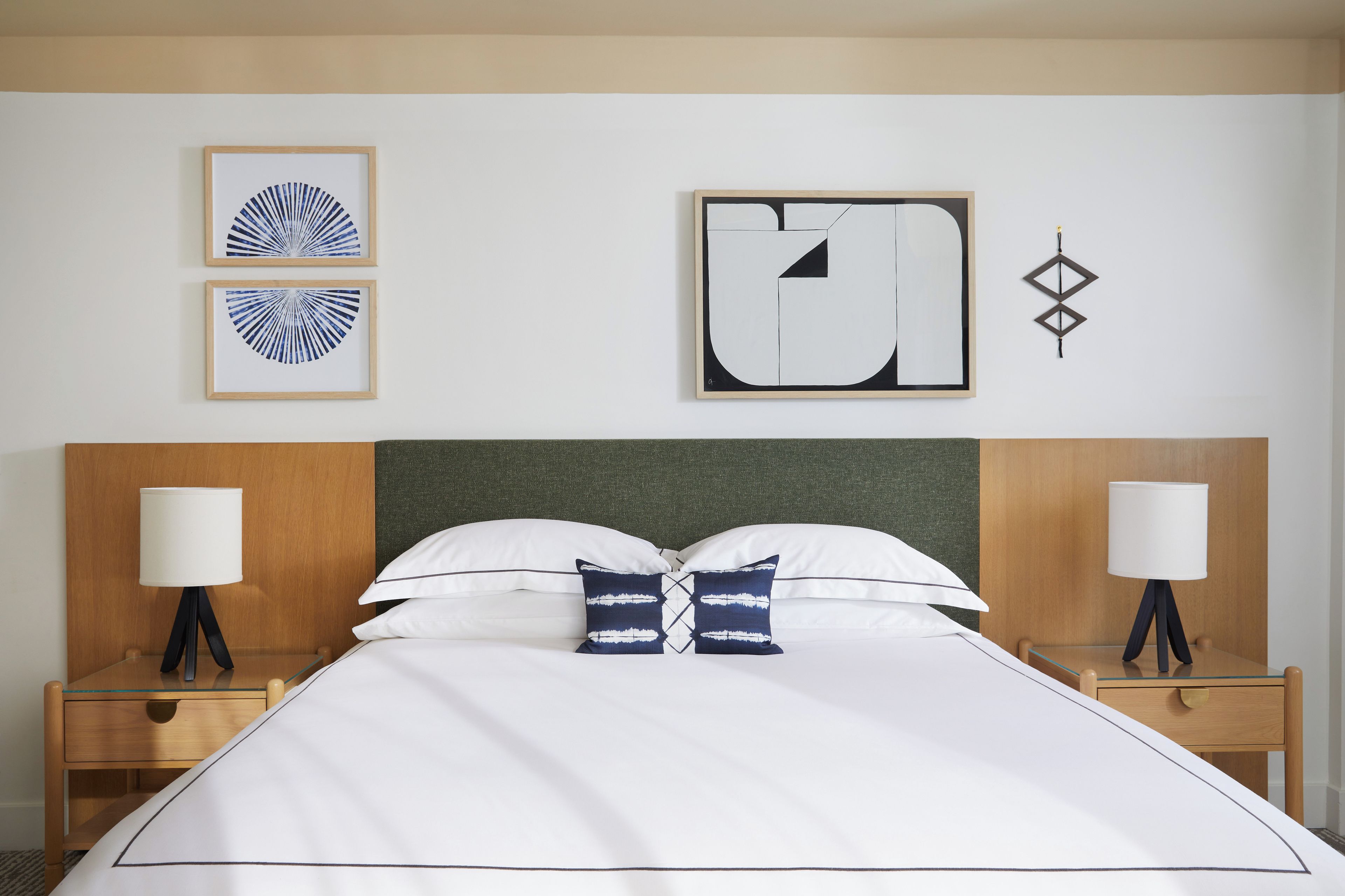 Ein ordentlich bezogenes Bett mit weißen Leinen und zwei Zierkissen, das von zwei Nachttischen mit Lampen gesäumt wird, in einem Zimmer mit schlichtem, klarem Design.