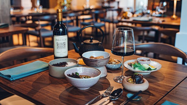 Una mesa de comedor con diversos platos, una botella de vino y una copa de vino tinto.