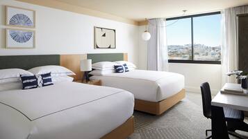 A hotel room with two beds, a desk, a chair, a lamp, and a view of the city.