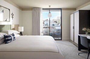A hotel room with a large bed, a desk, a chair, a lamp, a view of the city, and a balcony. - Kimpton Hotel Enso by IHG (San Francisco)