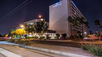 Un hotel moderno con un cartel llamativo, fachada bien iluminada y una zona ajardinada con palmeras.