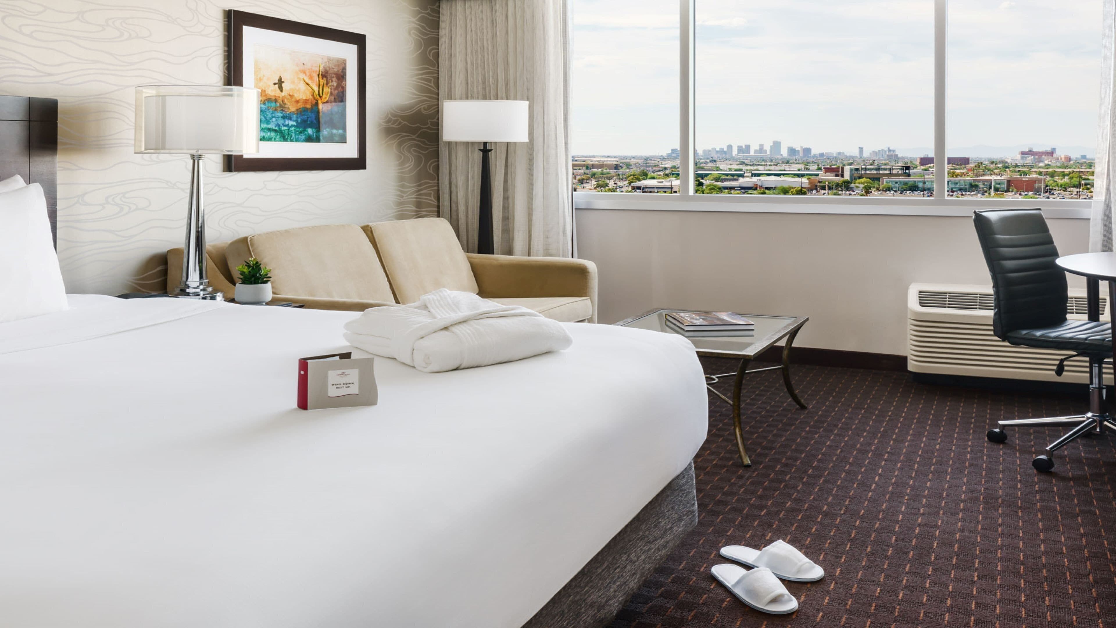 Ein Hotelzimmer mit Bett, Schreibtisch, Stuhl und Blick auf die Stadt, inklusive Fenster.