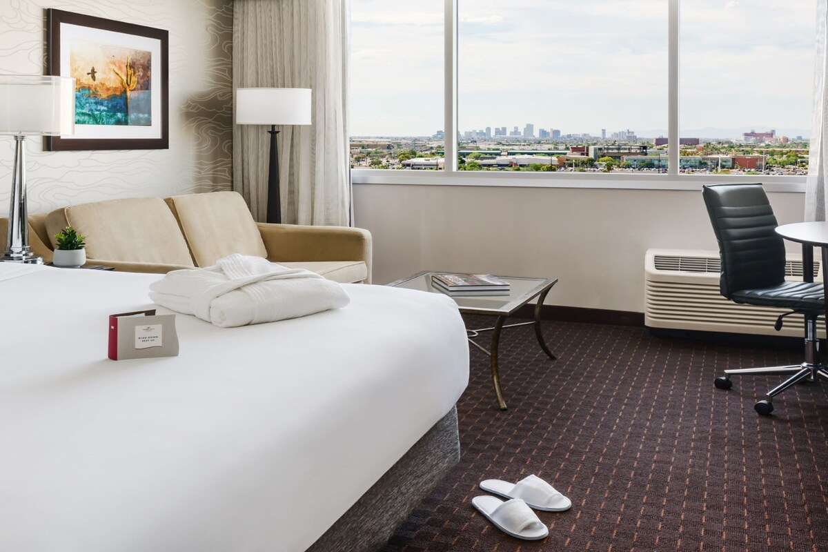 Habitación de hotel con una cama grande, un escritorio, una silla, vistas a la ciudad y un cuadro en la pared.