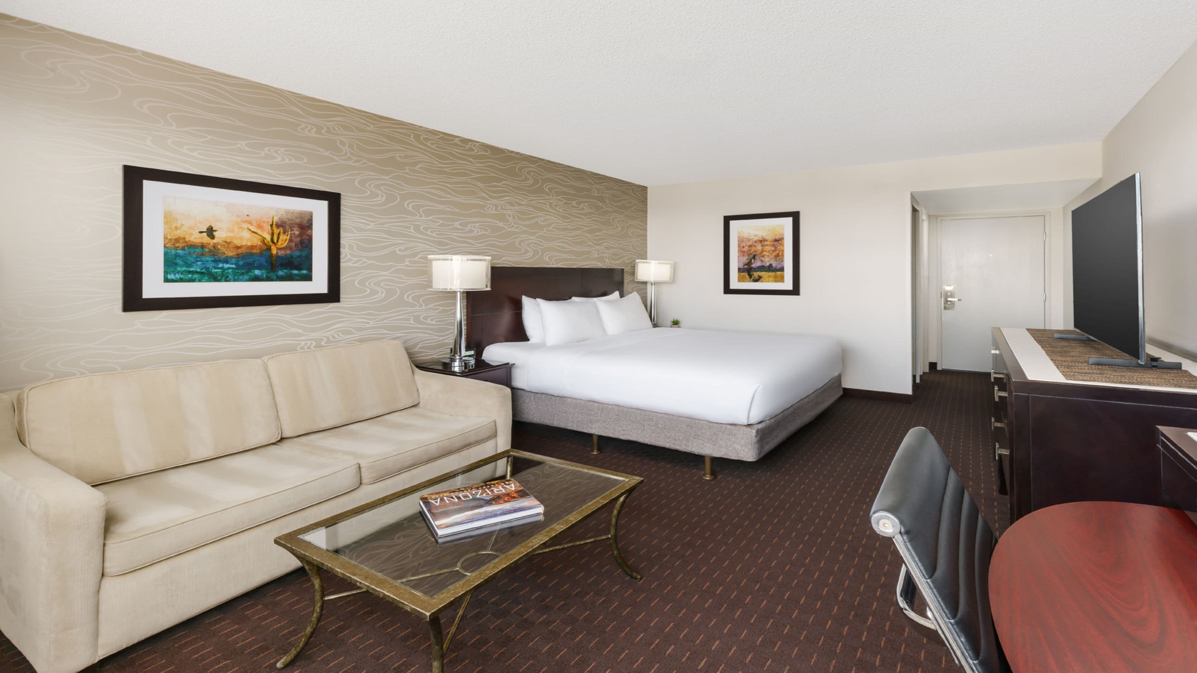 A hotel room with a bed, a sofa, a coffee table with a magazine, and two wall-mounted lamps.