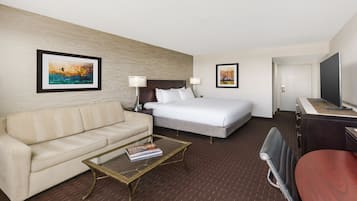 Habitación de hotel con cama, sofá, mesita de centro con una revista y dos lámparas de pared.