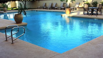 Una piscina con sillas de descanso y una mesa, rodeada de plantas en macetas.