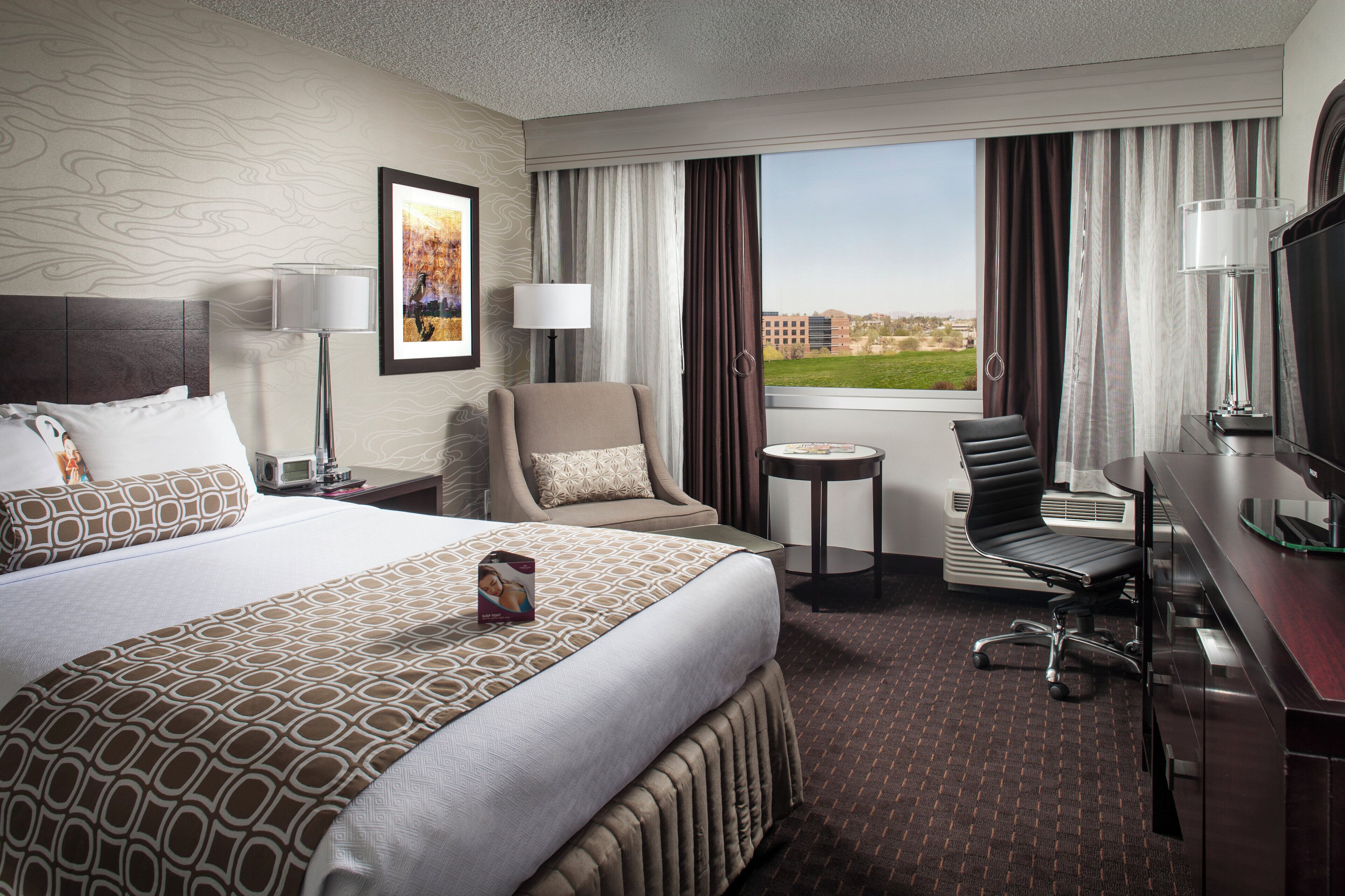 A hotel room with a large bed, a desk, a chair, a small table, and a window with a view.