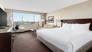 A hotel room with a large bed, a desk with a chair, a sofa, a TV, and a window with a city view. - Crowne Plaza Phoenix Airport - PHX by IHG (Phoenix)