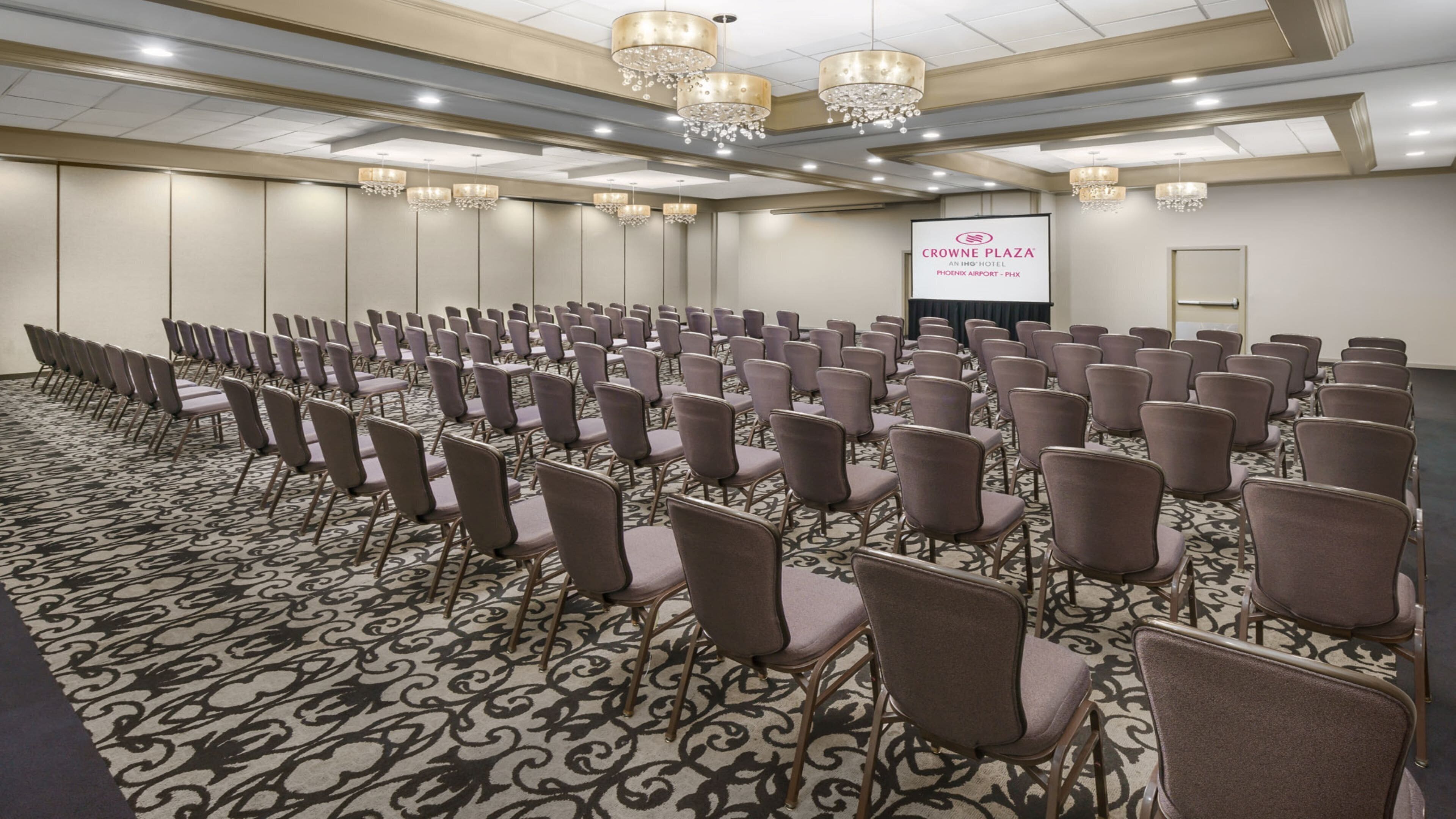 Un salón de conferencias con filas de sillas, una pantalla de proyector y candelabros.