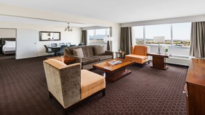 A hotel room with a sofa, armchairs, a coffee table, a desk, and a view of the city. - Crowne Plaza Phoenix Airport - PHX by IHG (Phoenix)