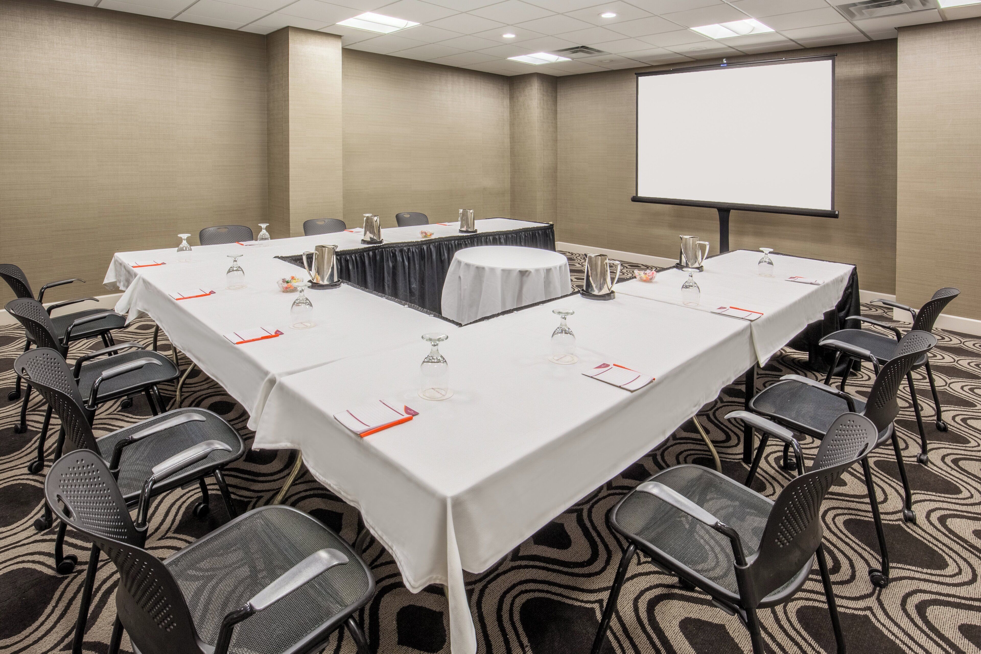 A conference room with a long table, chairs, and a projector screen.
