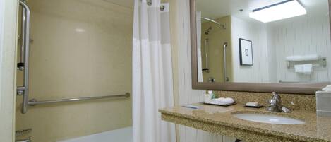 Un baño con bañera, ducha con barra de apoyo, lavamanos con tocador y espejo.
