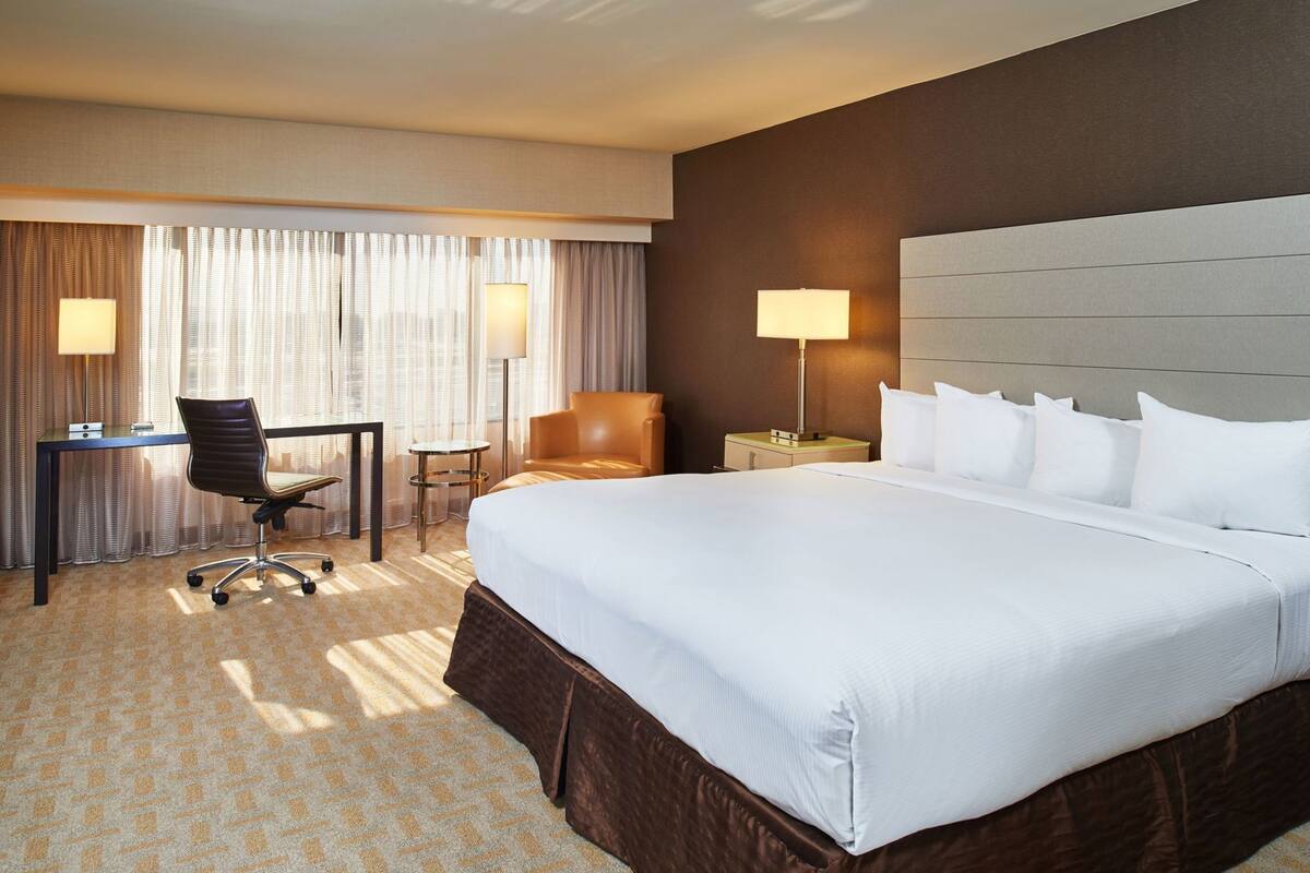 A hotel room with a large bed, a desk, a chair, and two lamps.