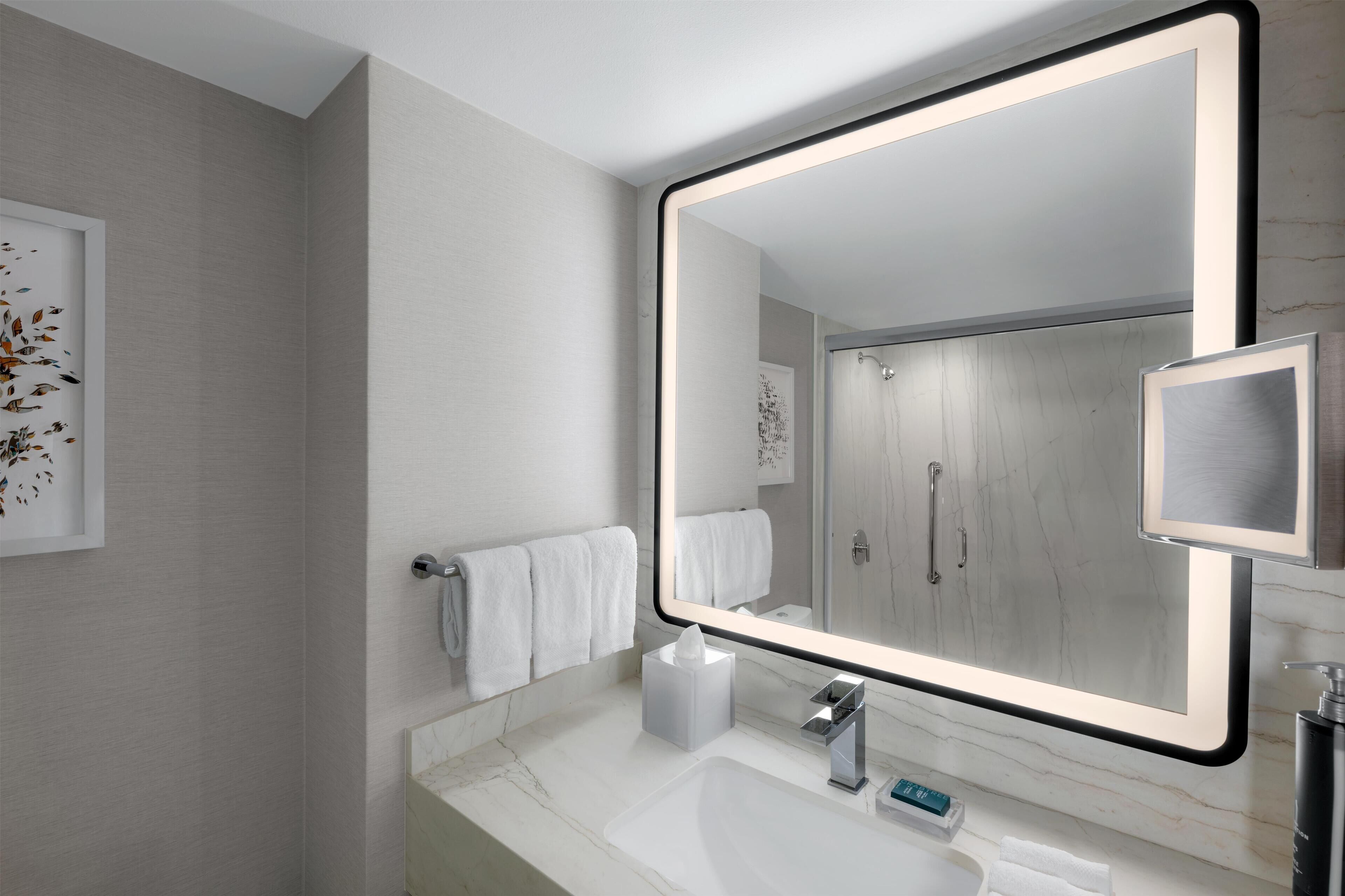 Een moderne badkamer met een grote spiegel, een witte marmeren countertop en een handdoekrek.