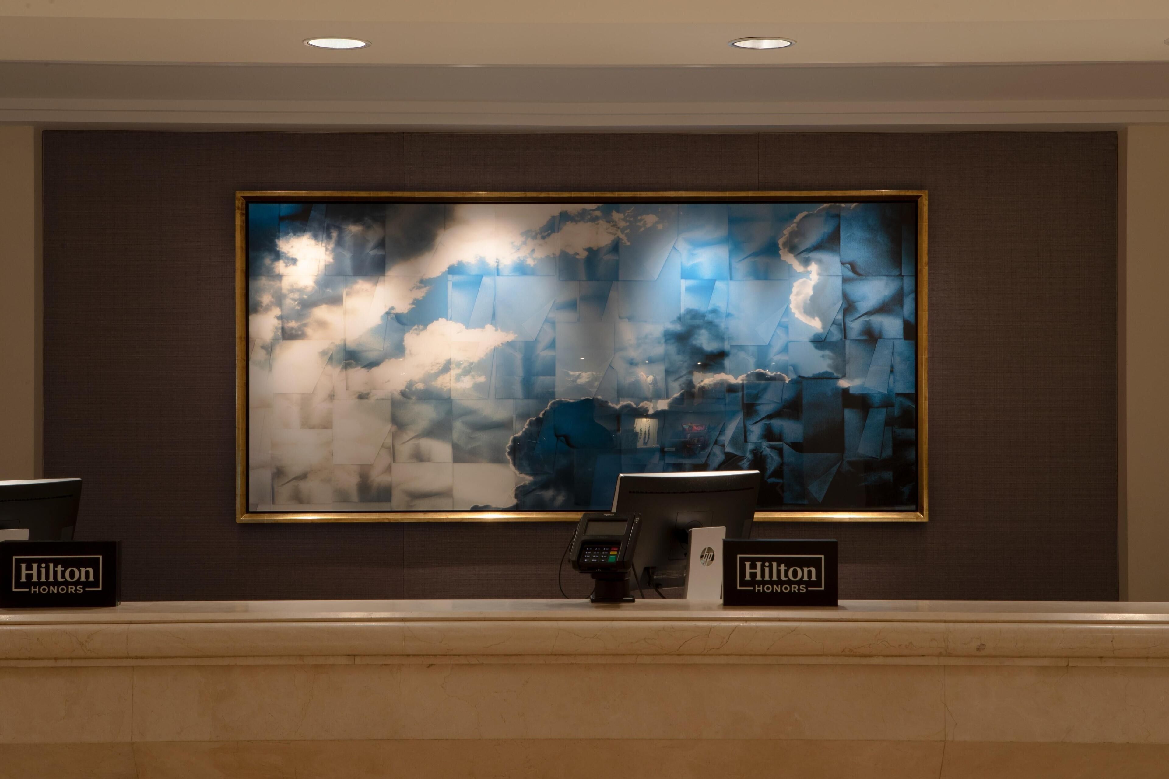 A reception desk with a large abstract painting above it, two 'Hilton Honors' plaques, and a modern design with a marble countertop.