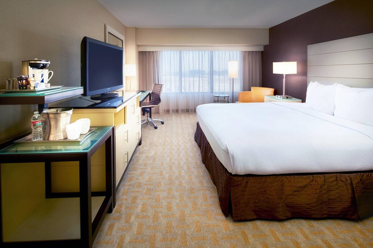 A hotel room with a large bed, a desk with a television, a coffee maker, and a chair.