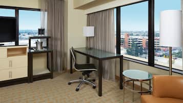 Een hotelkamer met een bureau, stoel, televisie en uitzicht op de stad.