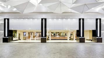 Um hall amplo com design geométrico no teto, pilares grandes e piso de azulejos.