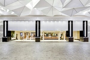 Um hall amplo com design geométrico no teto, pilares grandes e piso de azulejos.