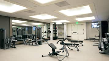 Een sportschool met diverse fitnessapparaten, banken en een spiegelwand.