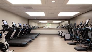 A gym with multiple treadmills and elliptical machines arranged in rows.