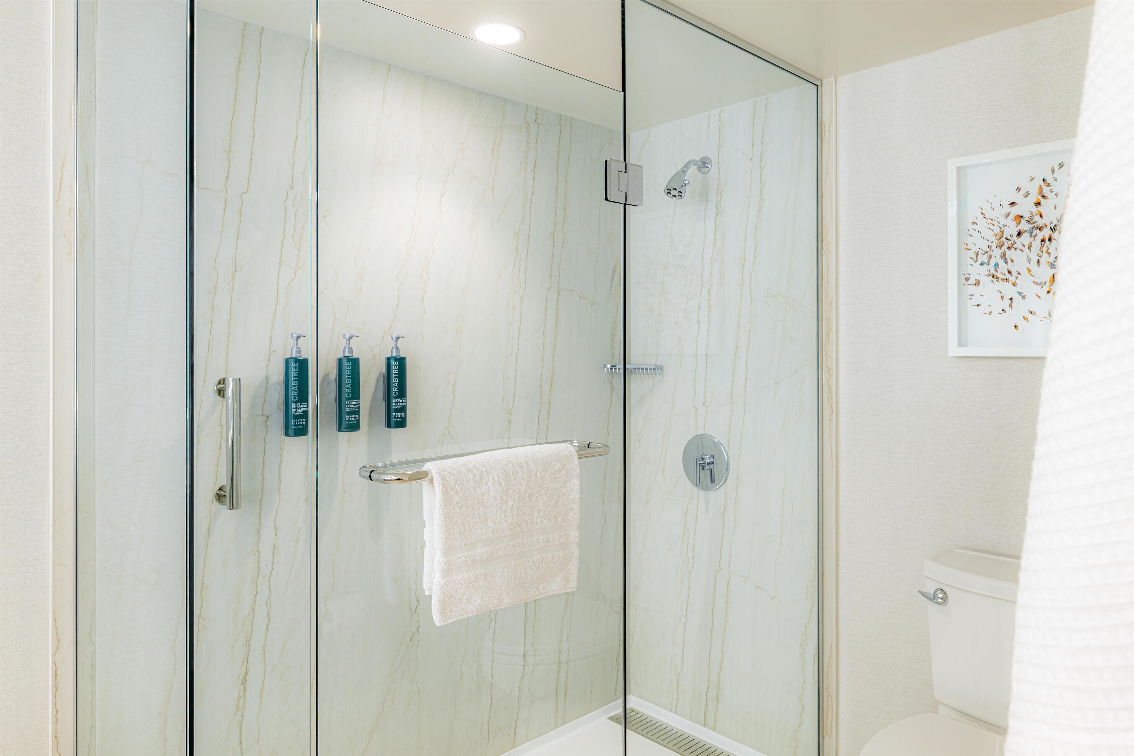 A modern bathroom with a glass-enclosed shower, a white toilet, and a framed artwork on the wall.