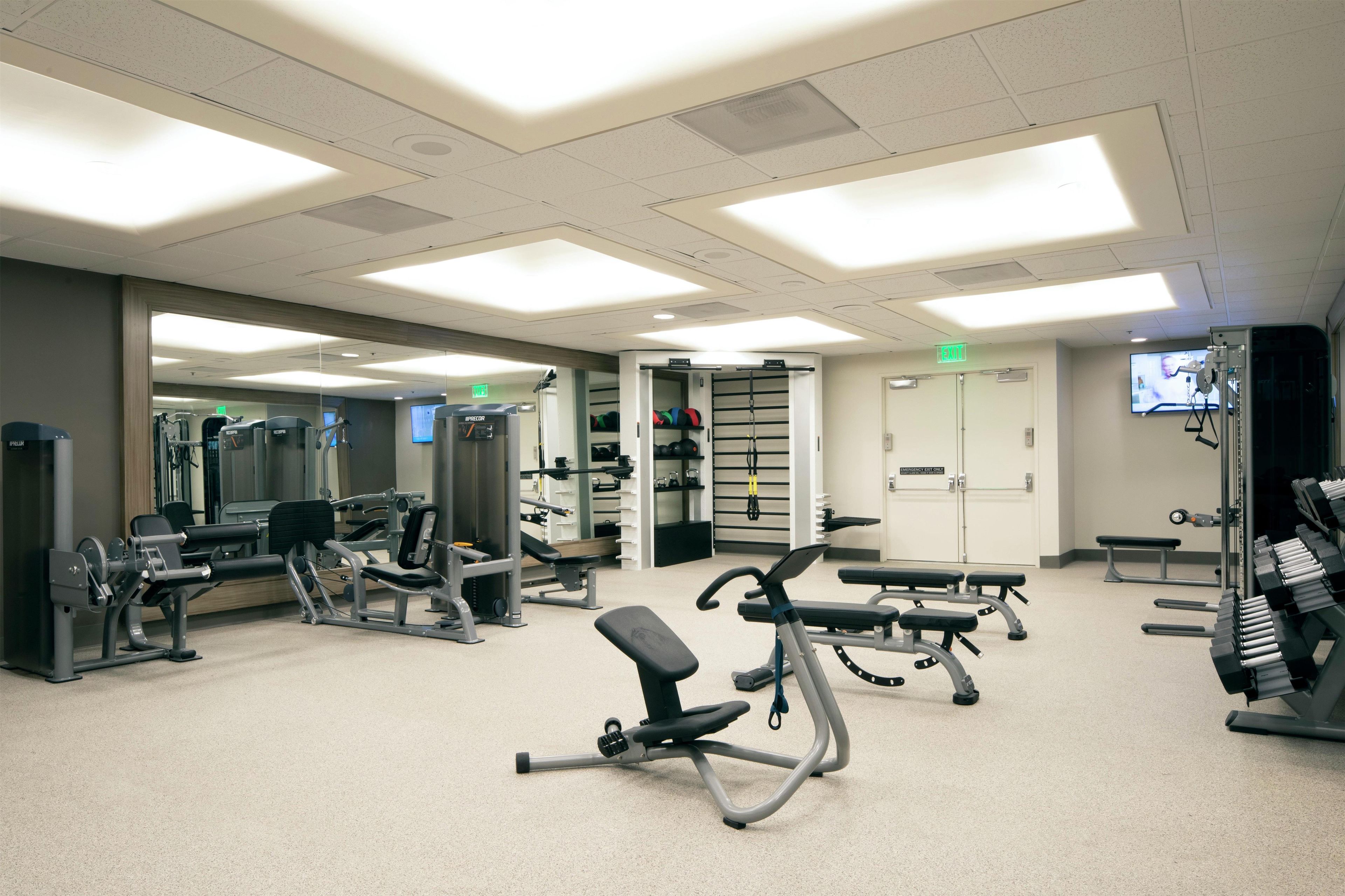 A gym with various exercise machines, benches, and a mirrored wall.