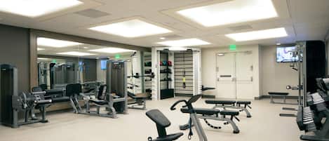 Un gimnasio con diversas máquinas de ejercicio, bancos y un espejo grande.